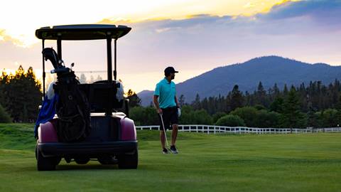 A golfer near a golf cart at dusk looking at the course